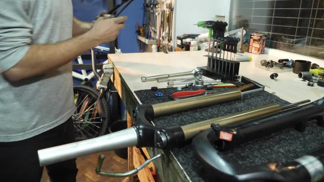 A man bike mechanic with a beard assembles a mountain bike in his workshop.