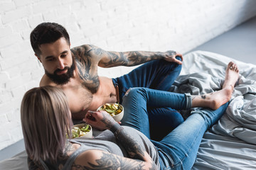 pregnant tattooed girlfriend eating salad with boyfriend at home