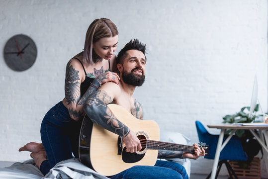 tattooed boyfriend playing guitar for girlfriend at home