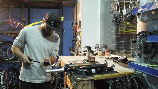 A man bike mechanic with a beard assembles a mountain bike in his workshop.