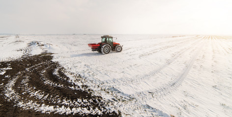 Farmer with tractor seeding - sowing crops at agricultural fields in winter