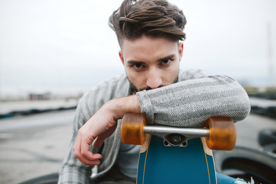 Young hipster stylish bearded man sitting on tires leaning on a longboard