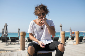 Stylish man sitting near the beach and smoking.