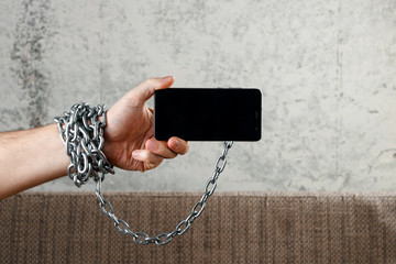 Close-up, the man's hand is tied with a chain to the smartphone. The concept is dependent on technology, phone, social networks, blogger.