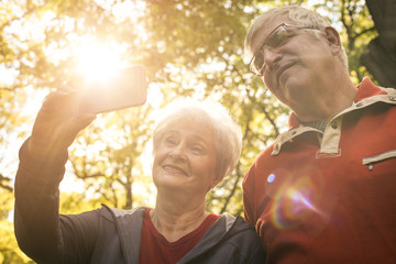 Seniors couple in sports clothing taking self picture in park.