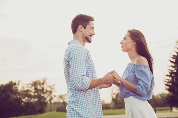 Fototapeta premium Side profile view of bearded brunet guy in checkered shirt, bonding dreamy lady, looking deep into eyes of each other. Leisure, chill, lawn stroll, relax lifestyle, well dressed stylish partners