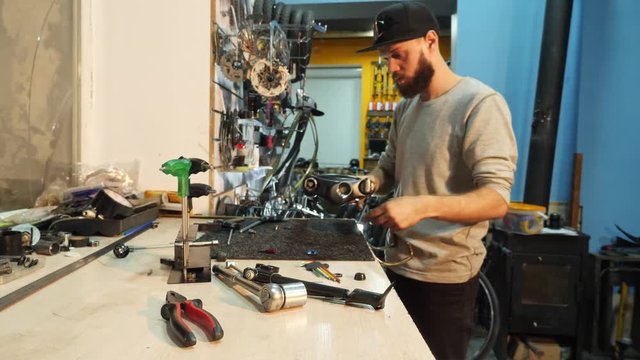 A man bike mechanic with a beard assembles a mountain bike in his workshop.