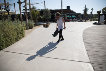 Stylish man walking down the street with a skateboard.