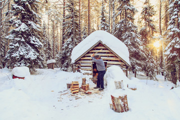 Man chopping wood in the forest near the hut.