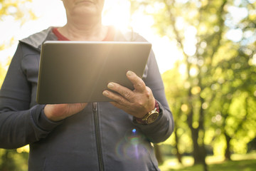 Senior woman in sports clothing using digital tablet in park.