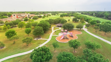 Aerial urban park with playground and asphalt trails in Houston, Texas, America. Elevated view of slides and swings in the park surrounded by green trees near Notre Dame Church.