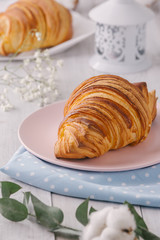 Delicious continental breakfast with fresh flaky french croissants, close up on the croissants. With white cotton flowers on a light wooden background. Provence rustic style
