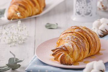Delicious continental breakfast with fresh flaky french croissants whith honey, close up on the croissants. With white cotton flowers on a light wooden background. Provence rustic style