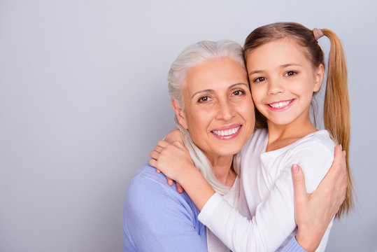Close up portrait of cute small lovely granddaughter and her charming nice kind granny they are hugging isolated on gray background copy-space