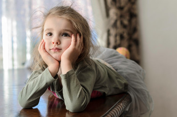 charming little girl lies on a wooden table, leaning on the palm of her chin