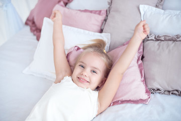 Obraz na płótnie Canvas Close-up little girl waking up with stretching arms while awake lying on white bed linen.