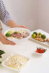 Female chef prepare traditional Vietnamese soup Pho bo with herbs, meat, rice noodles