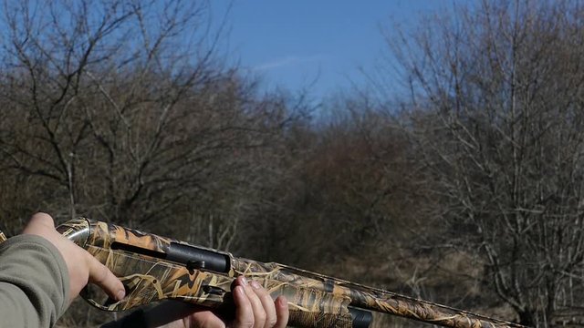 A camouflaged shotgun makes a shot. Cartridges fly out of the trunk. Slow motion.