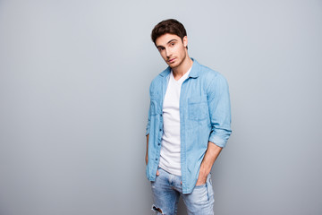 Fototapeta na wymiar Manly, masculine man in jeans outfit, holding hands in pockets of pants, looking at camera, standing over gray background
