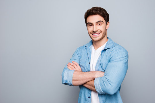Portrait with copy space, empty place of stunning, sexy, smiling, cool man in jeans shirt having his arms crossed, looking at camera, isolated on grey background