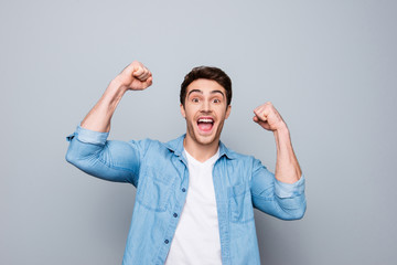 Portrait of lucky, attractive, excited, glad man with wide open mouth and raised arms looking at camera celebrating successfully passed exams, completed work, isolated on grey background