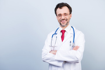 Vertical portrait of excited cheerful qualified expert specialist bearded experienced doctor wearing red tie classic white coat standing with folded arms isolated on gray background copyspace