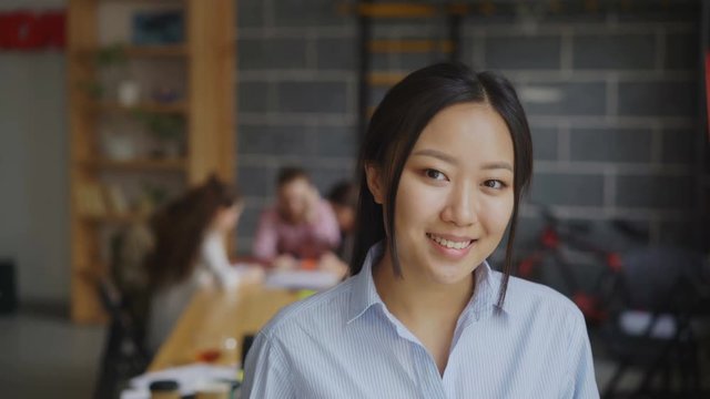 Portrait of asian confident businesswoman looking at camera and smiling while her multi-ethnic team working on start-up project in modern loft office