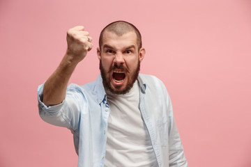 The young emotional angry man screaming on pink studio background