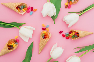 Pattern made of colorful bright candy in waffle cones and white flowers on pink background. Flat lay, top view