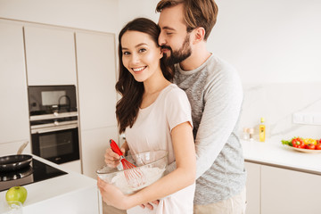 Smiling young couple whisking dough for pastry