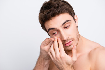Fototapeta premium Close up portrait of young, attarctive, muscular man putting contact lenses in his eye over white background