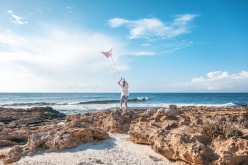 Beautiful happy young woman girl launches a kite at the seashore, sunshine vacation and joy concept