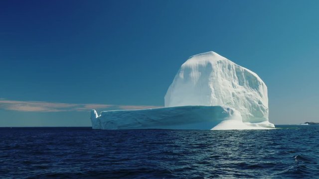 Tall and immense ice berg floating through blue arctic water