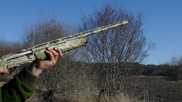 A camouflaged shotgun makes a shot. Cartridges fly out of the trunk. Skeet shooting. Slow motion.