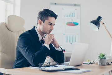 Half-turned portrait of focused confident busy hard-working leader smart clever intelligent handsome wearing formal dress-code sitting at the table reading information on the internet
