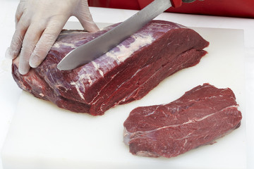 Closeup of the hands of a butcher cutting slices of raw meat off a large loin