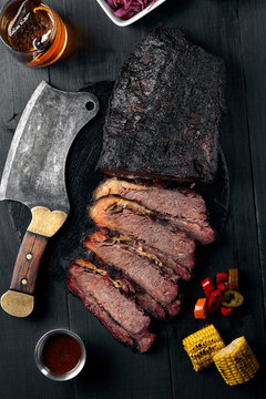 Fresh Brisket BBQ beef sliced for serving against a dark background with sauce, hot peppers and corn.
