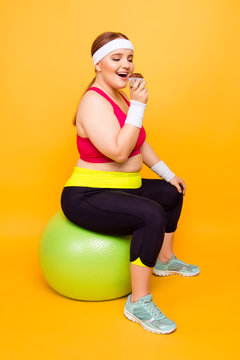 Young woman eats cupcake while sitting on exercise ball