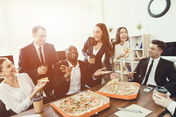 The office staff eat pizza and drink coffee in the business office.