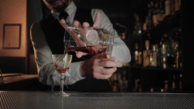Professional barista in exquisite bar or restaurant pours fancy alcoholic drink from tall glass to blend into vintage shot. Concept of vip treatment and luxuriuos lifestyle or fich and famous