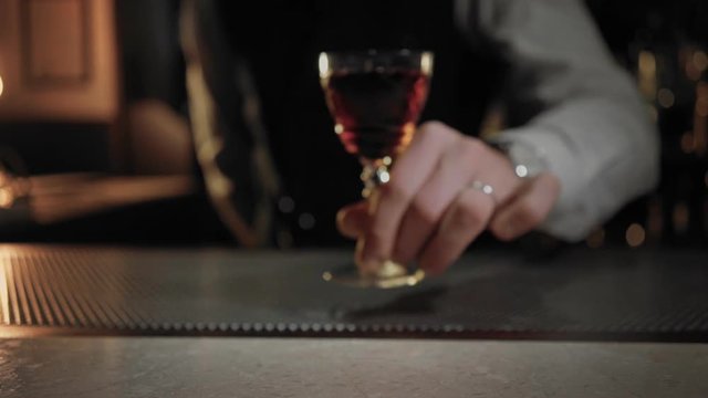 Professional bartender serves drink or alcoholic cocktail to client or customer, from out of focus, pov shot of someone recieving order at high end classy establishment