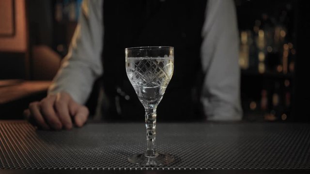Professional bartneder serves customer ordered drink in vintage and retro unique glass, dry martini or vodka, puts in little sword with pickled olive for distinguished taste and flavor