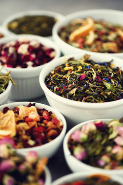 Assortment Of Dry Tea In White Bowls. Tea Types Backgound: Green, Black, Floral, Herbal, Mint, Melissa, Ginger, Apple, Rose, Lime Tree, Fruits, Orange, Hibiscus, Raspberry, Cornflower, Cranberry