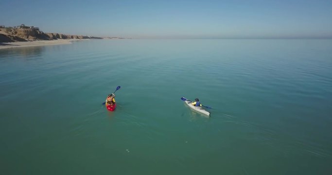 Two female kayakers paddling into the distance as the drone gets closer to them.