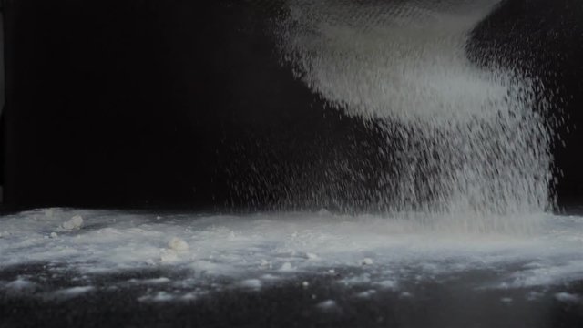 sift flour through a sieve. Slow-motion shooting. Black background, isolated. Side from the side