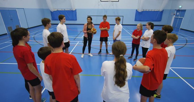 4K Sports teacher with young pupils on school basketball court, giving team talk before a game