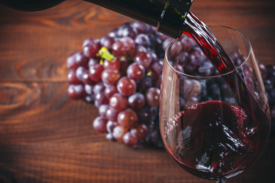Bottle and glass of red wine, grape and cork on wooden background.