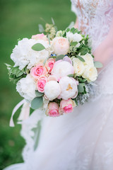 Gorgeous bride holds rich wedding bouquet of pink and white peonies and roses
