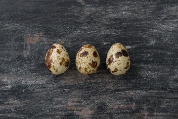 Three quail eggs on a black gray vintage background