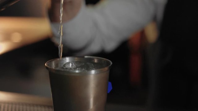 Close up focus, unrecognizable bartender pours vodka from one shaker to another steel shaker with ice to cool down and mix it with other alcohol before serving. Bar life style routine concept